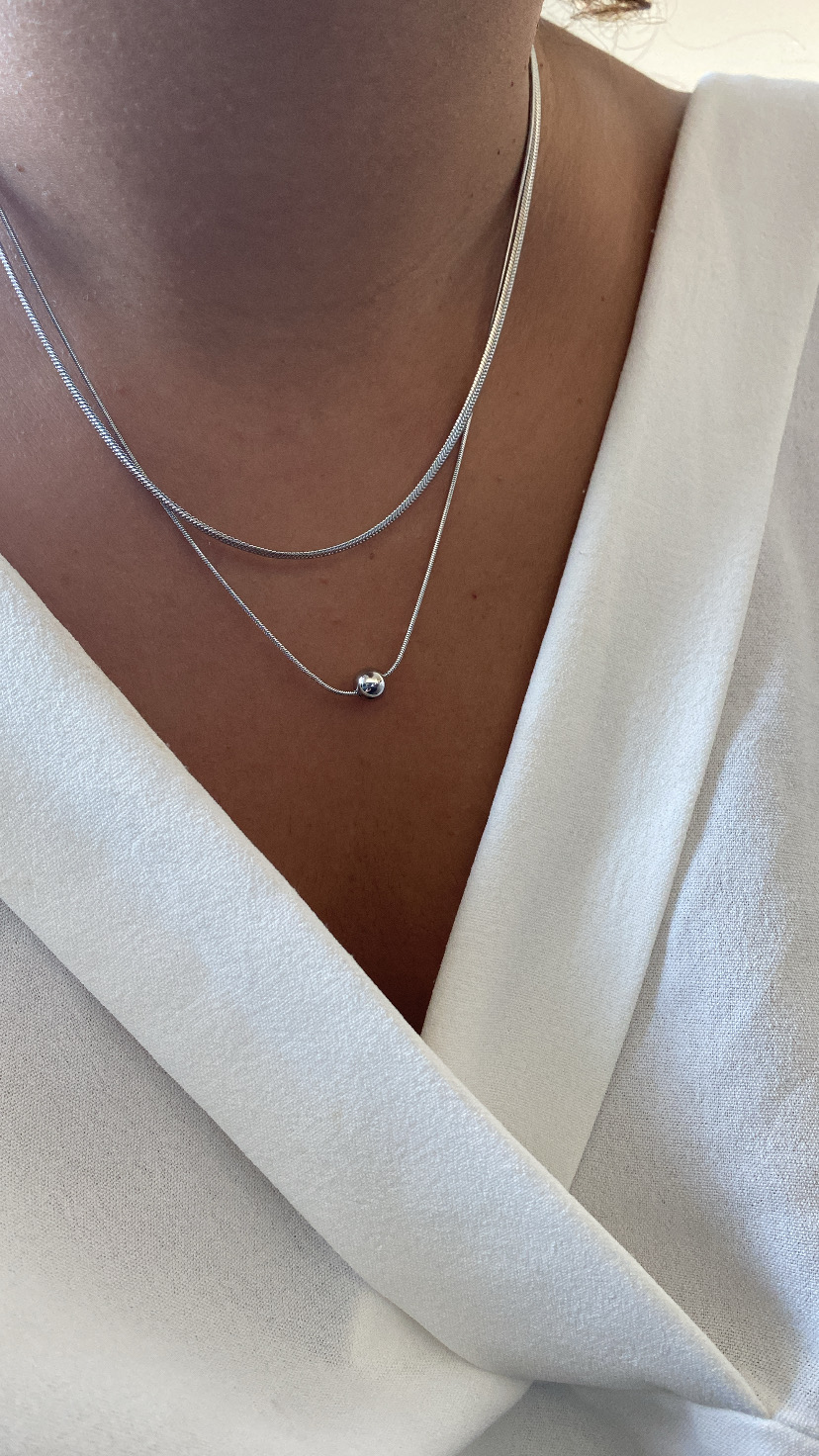 Colar duplo prateado com pendente esférico sobre roupa branca