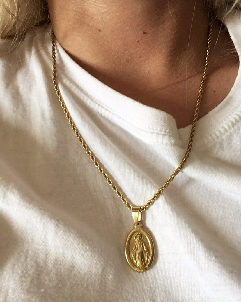 Colar dourado com pingente religioso usado numa t-shirt branca