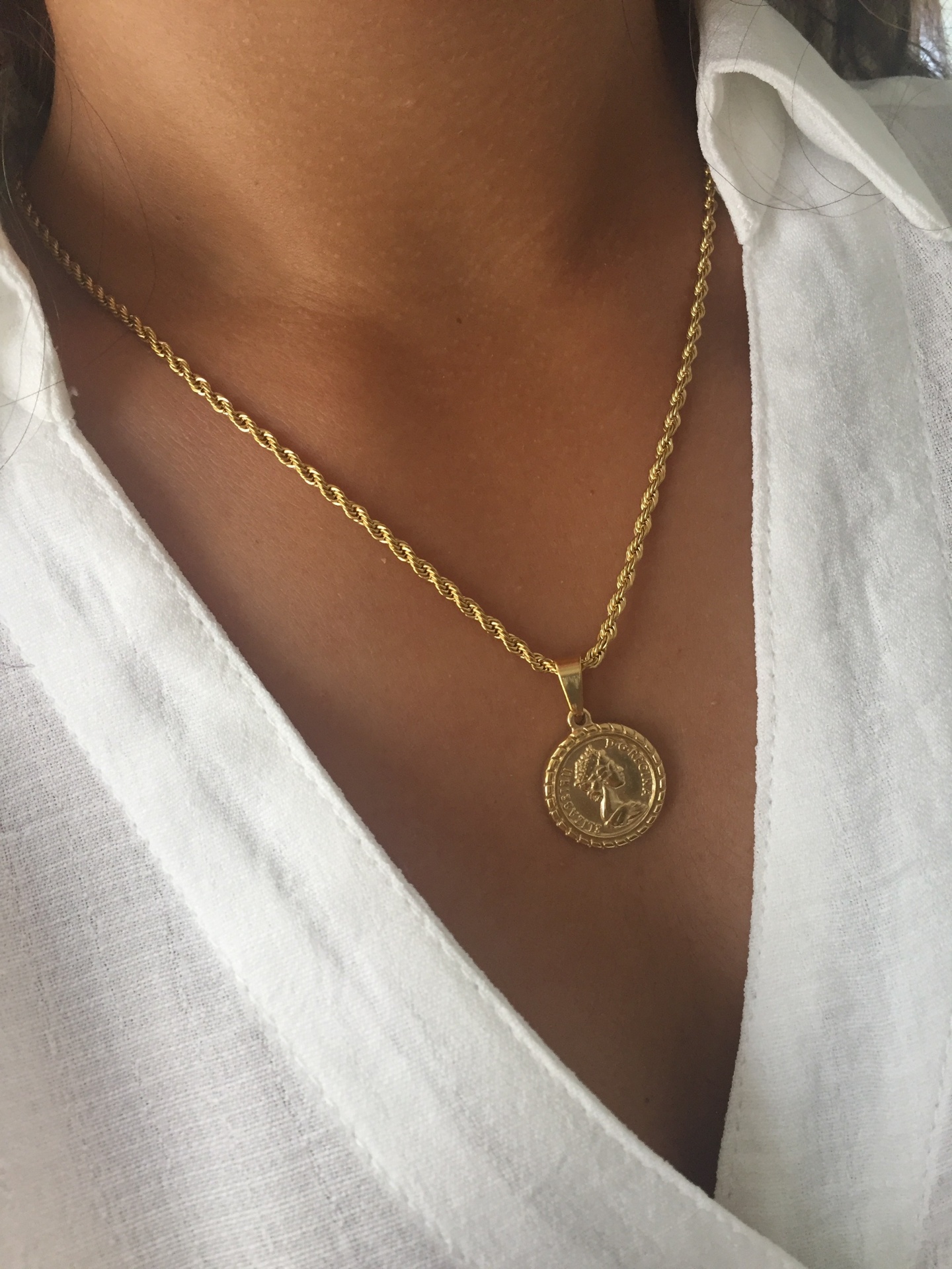Colar dourado com pendente redondo em relevo usado com camisa branca