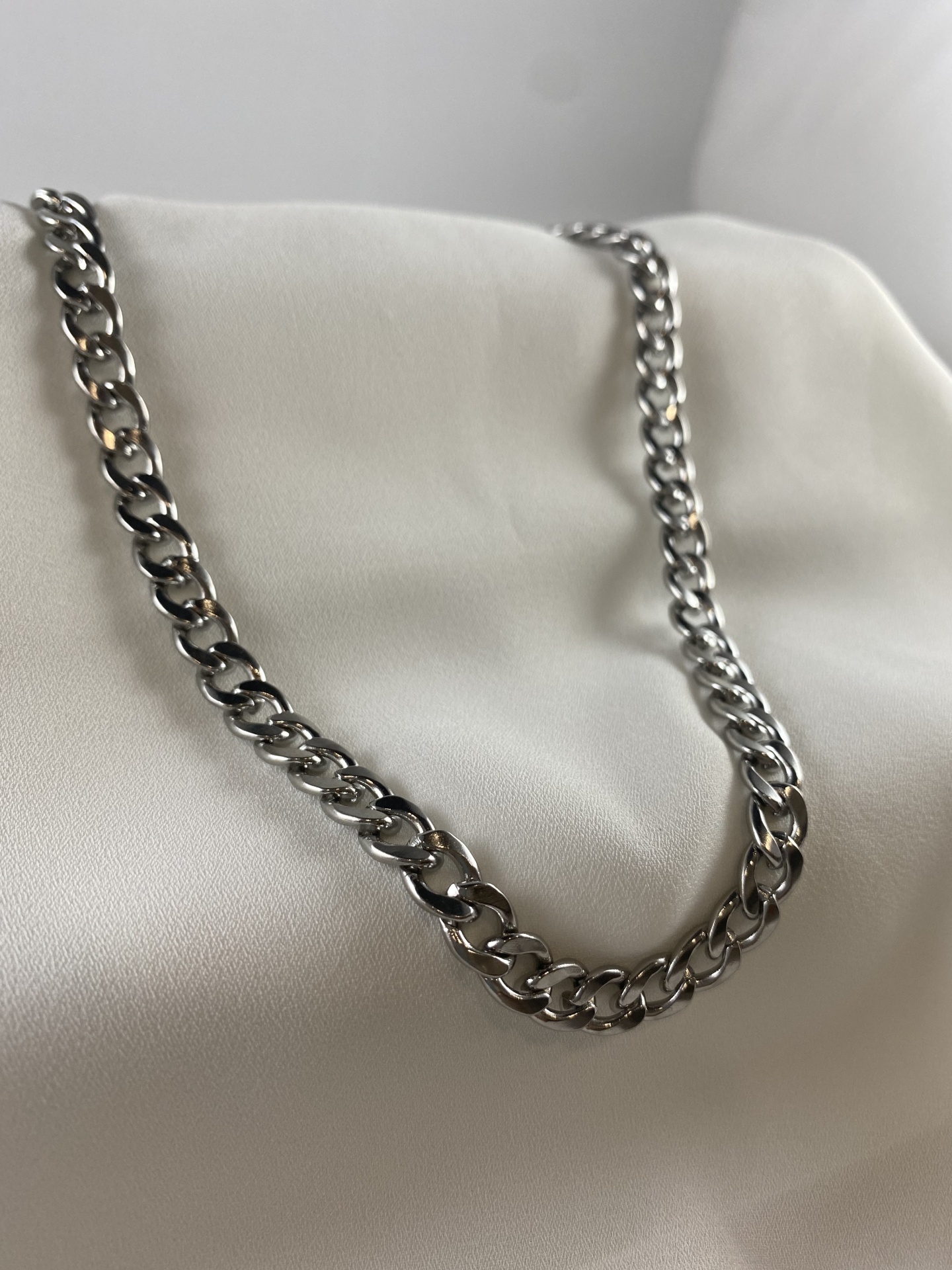 Colar prateado de corrente com elos grossos sobre superfície branca