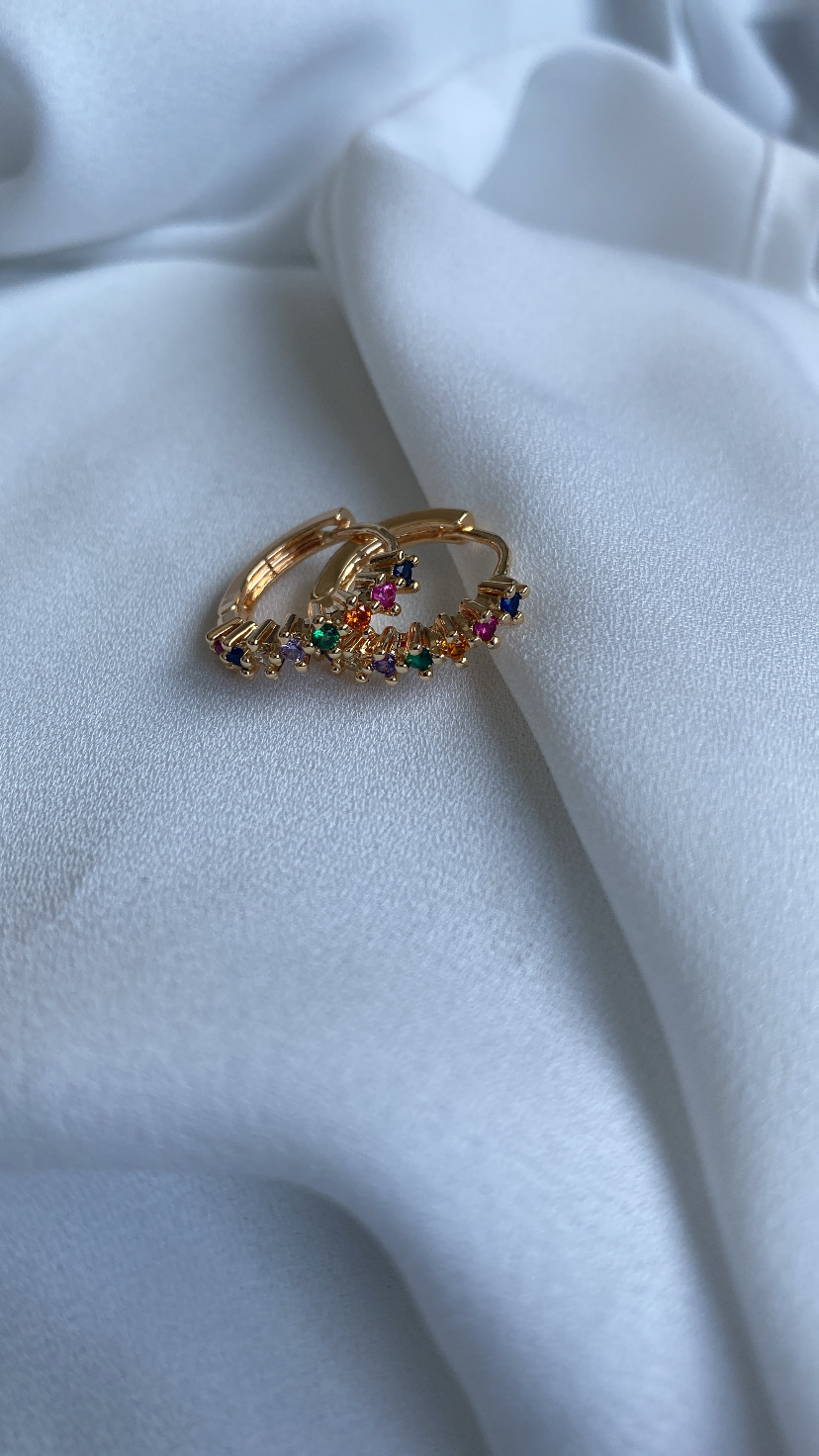 Brincos de argola dourados com pedras coloridas sobre tecido branco