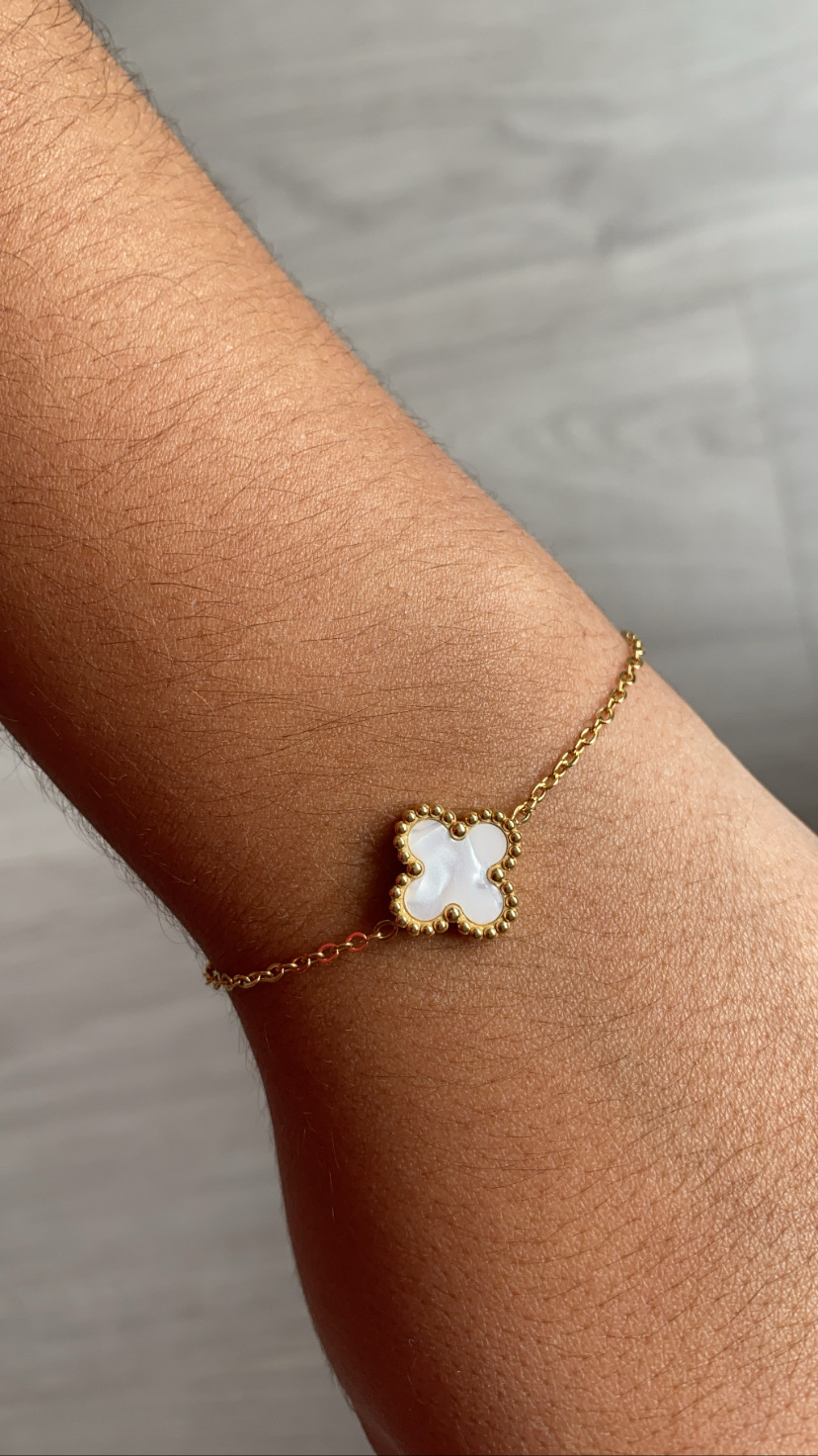 Pulseira dourada com pendente de flor madre-pérola no pulso.