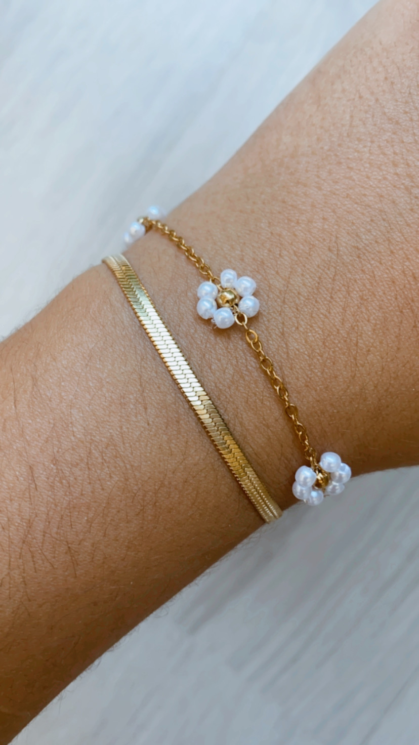 Pulseira dupla dourada com flores de pérolas brancas num pulso