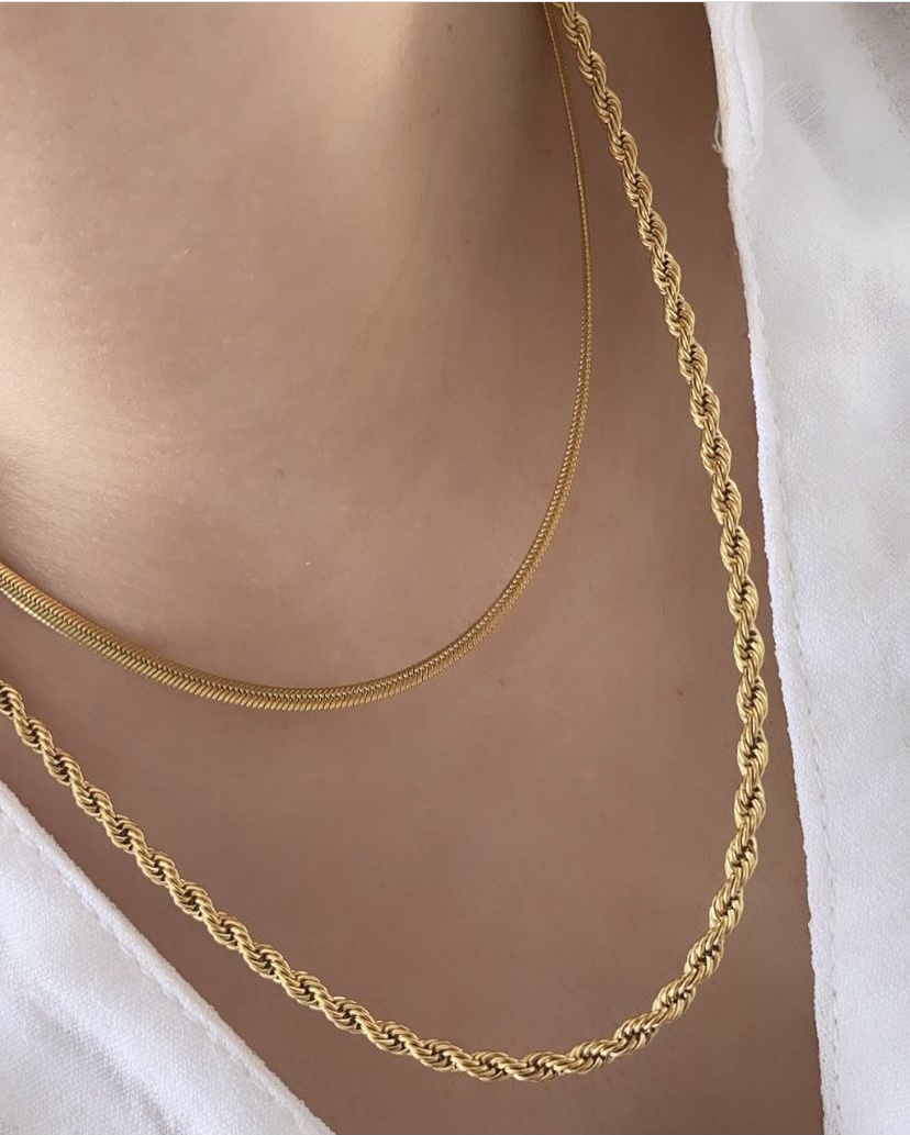 Dois colares dourados, um fino liso e um grosso entrelaçado, em pescoço com roupa branca
