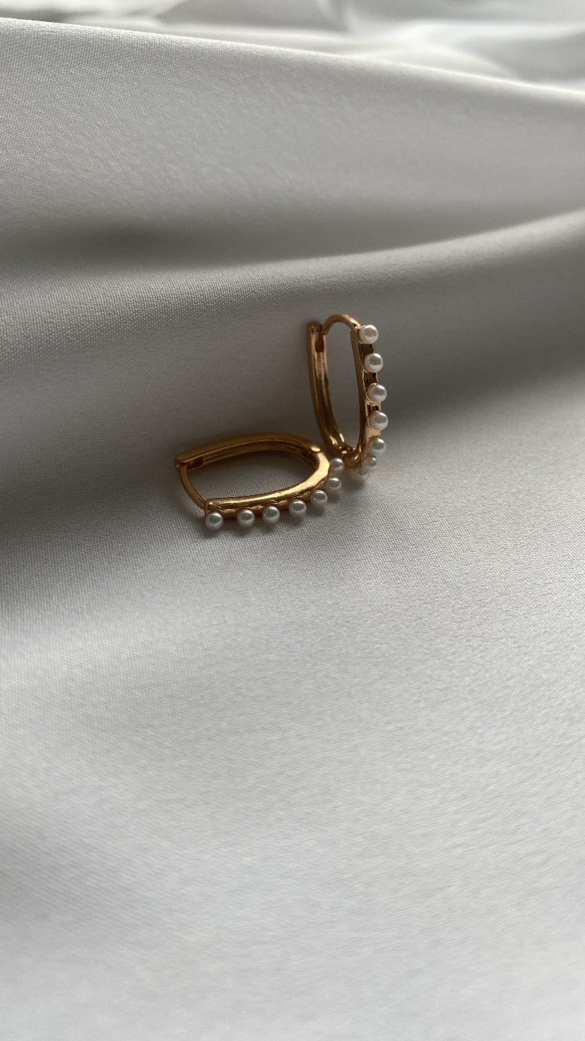 Brincos dourados com pérolas sobre tecido branco