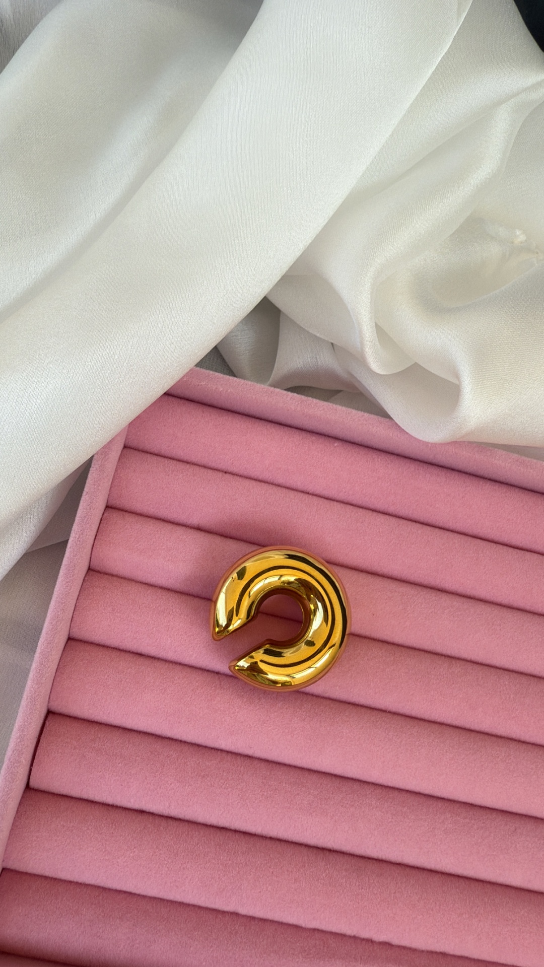 Anel ou pulseira dourada em almofada rosa de veludo com tecido branco ao fundo