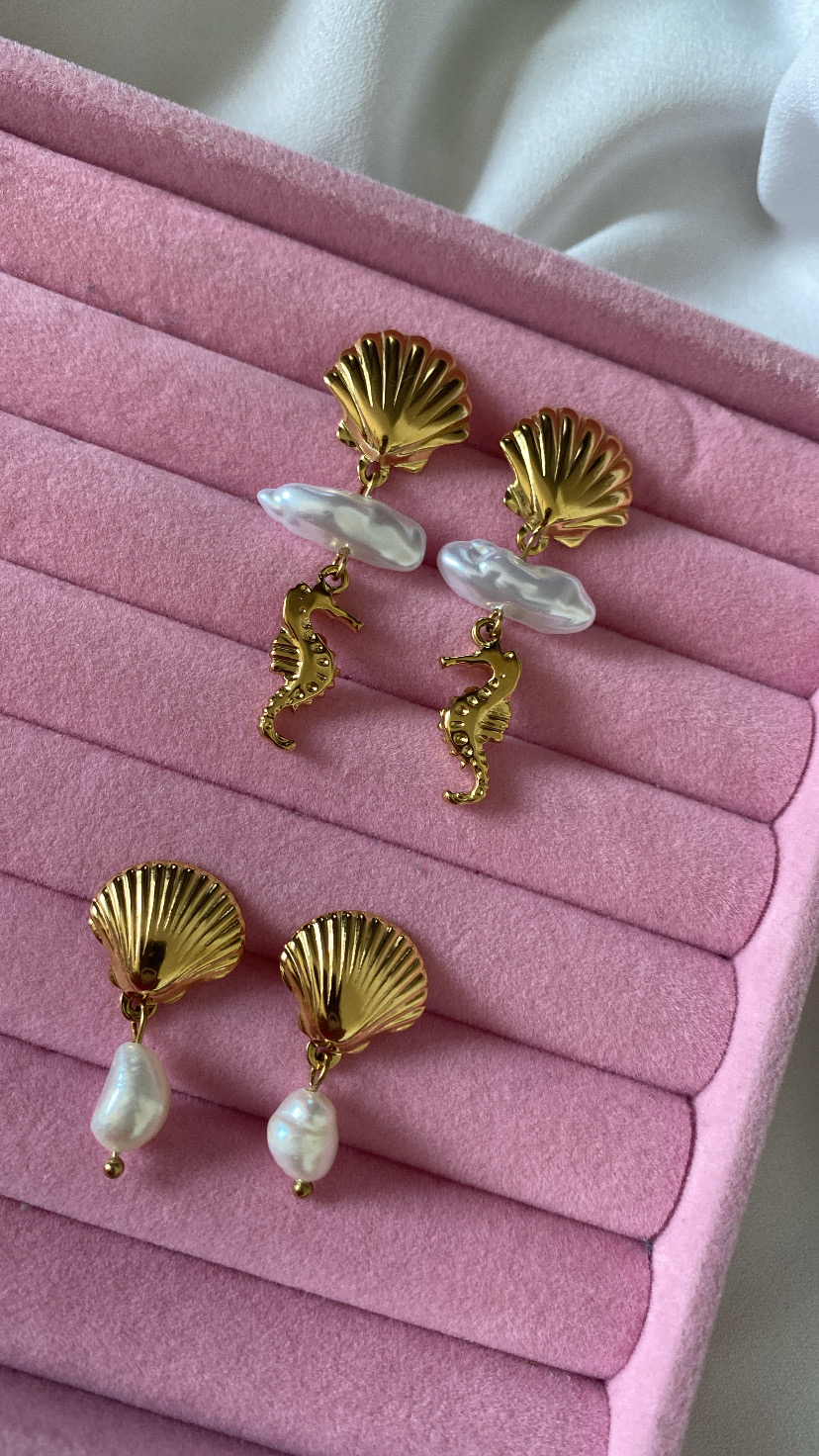 Dois pares de brincos dourados com conchas e pérolas sobre estojo rosa