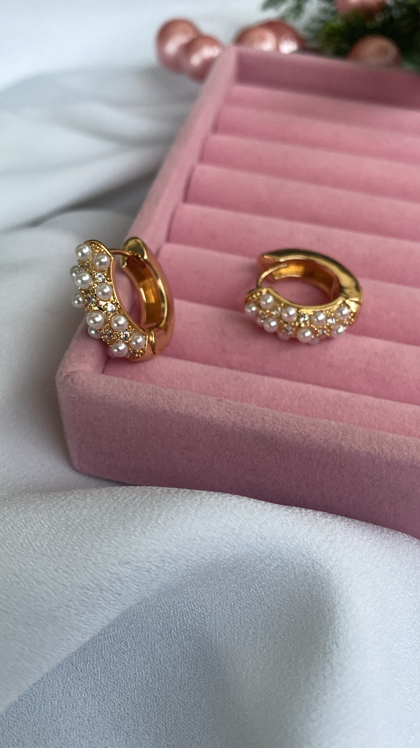 Brincos dourados com pérolas numa caixa rosa sobre tecido branco