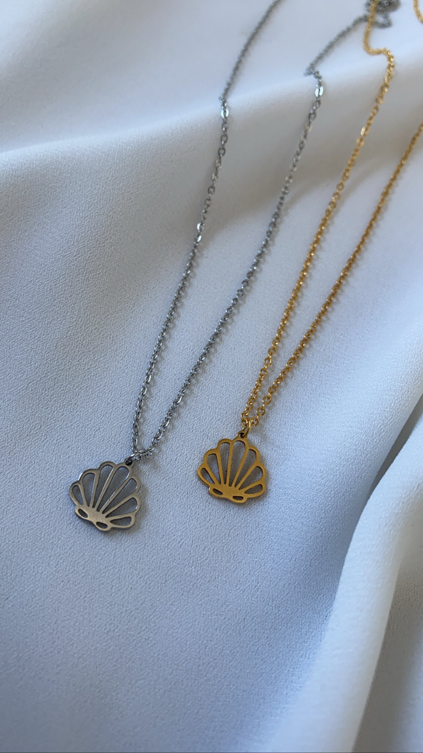 Colares com pendentes em forma de concha, um prateado e outro dourado sobre tecido branco