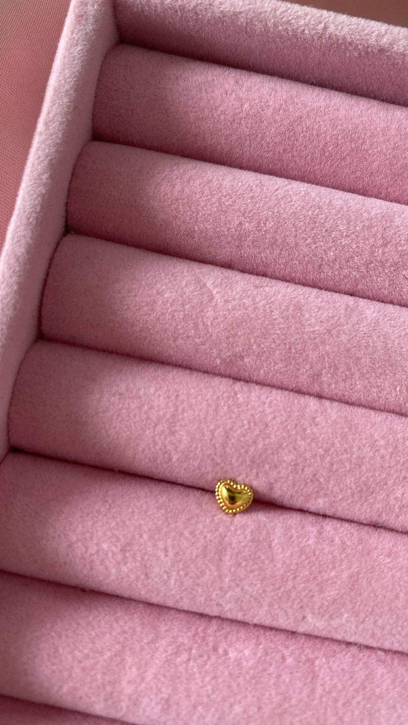 Anel dourado em forma de coração numa caixa de veludo rosa com rolos para anéis