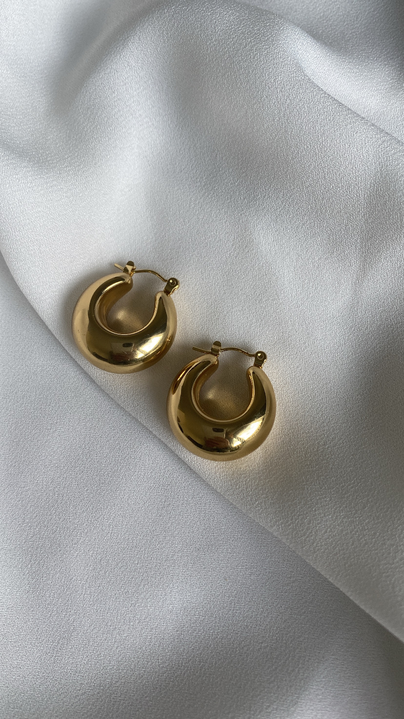 Brincos dourados tipo argola sobre tecido branco