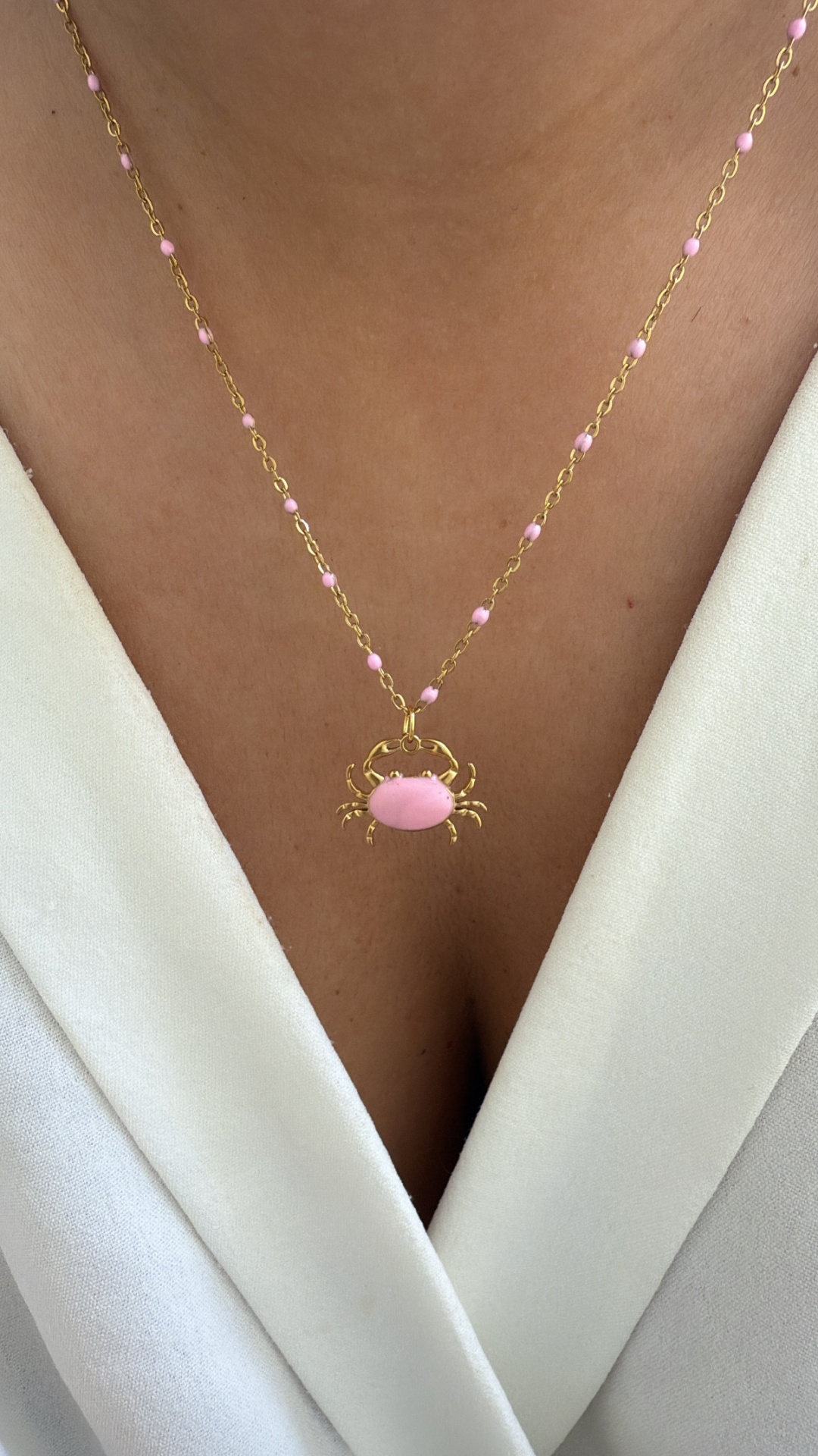 Colar dourado com pendente de caranguejo cor-de-rosa sobre roupa branca
