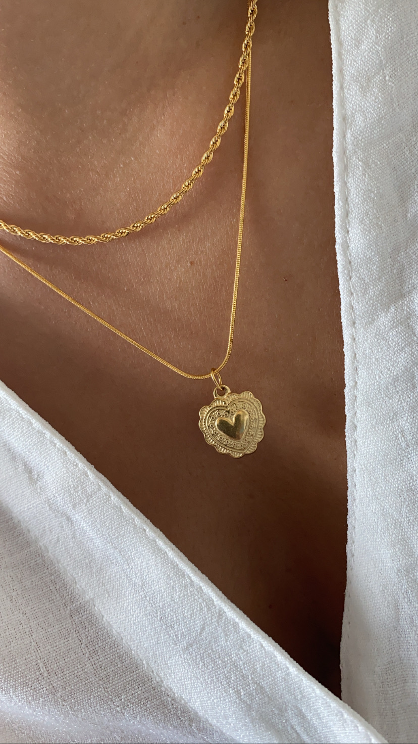 Colar dourado com pingente de coração usado sobre pele e roupa branca