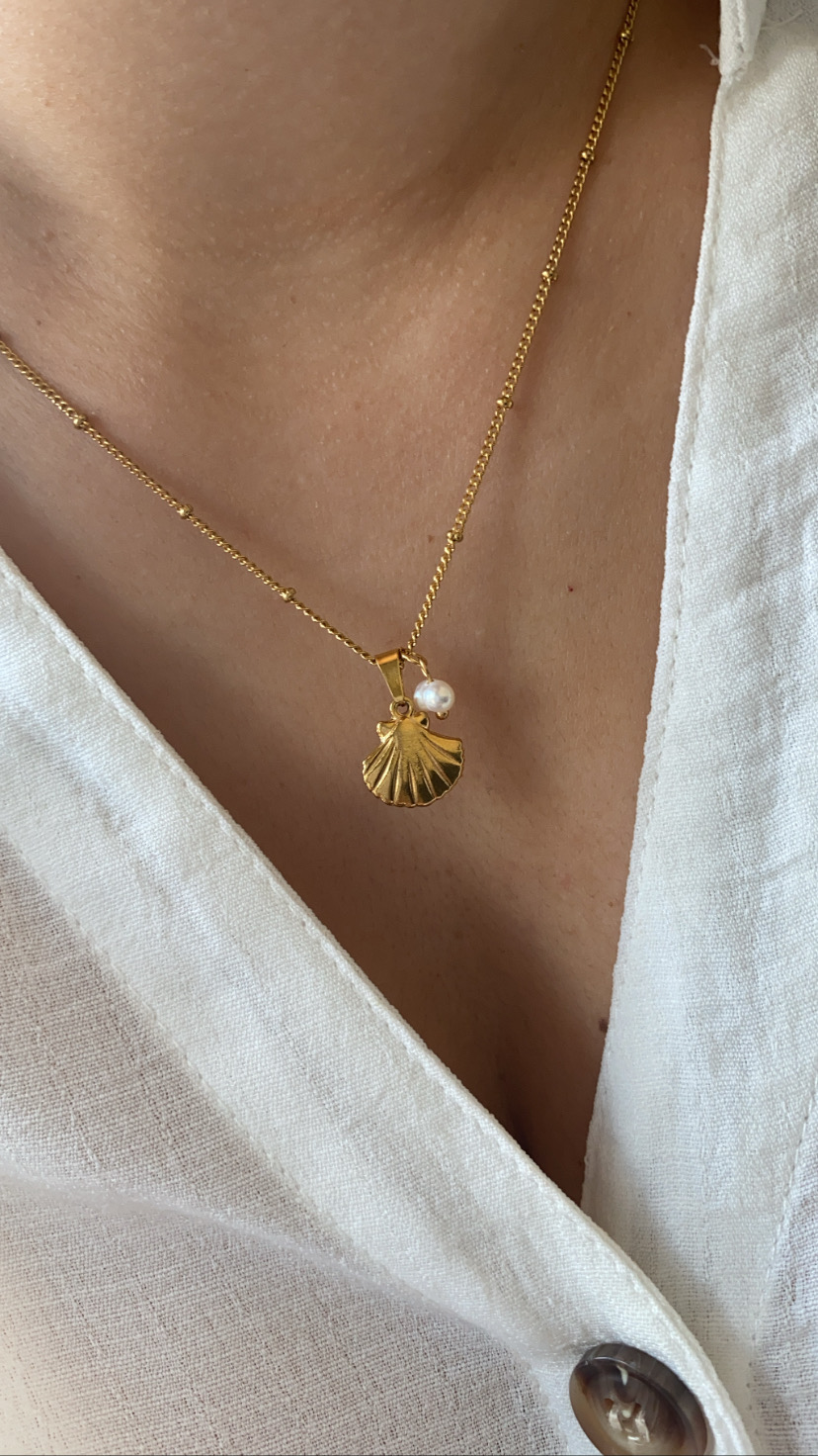 Colar dourado com pendente de concha e pérola com camisa branca