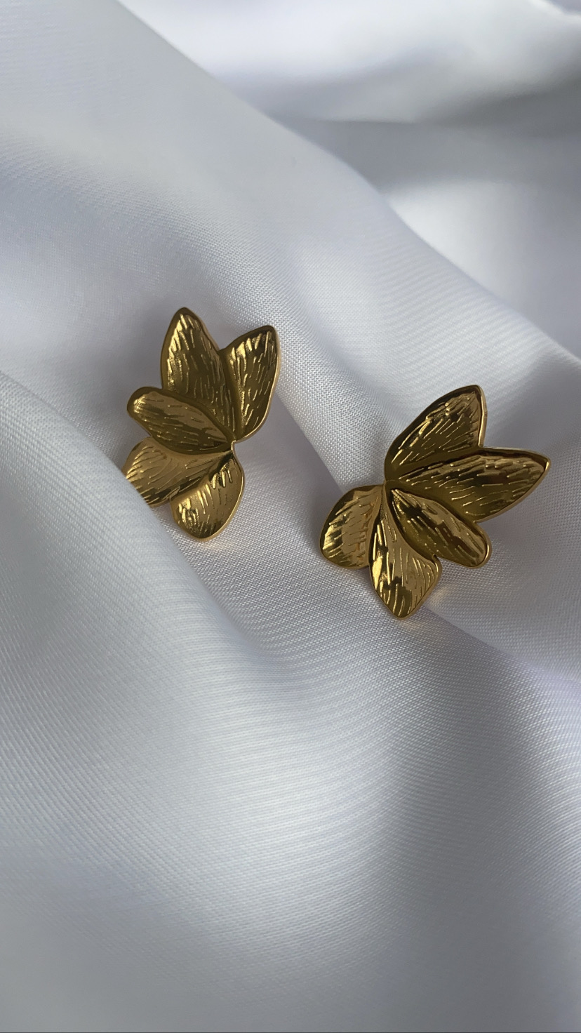 Brincos dourados em forma de folhas sobre tecido branco