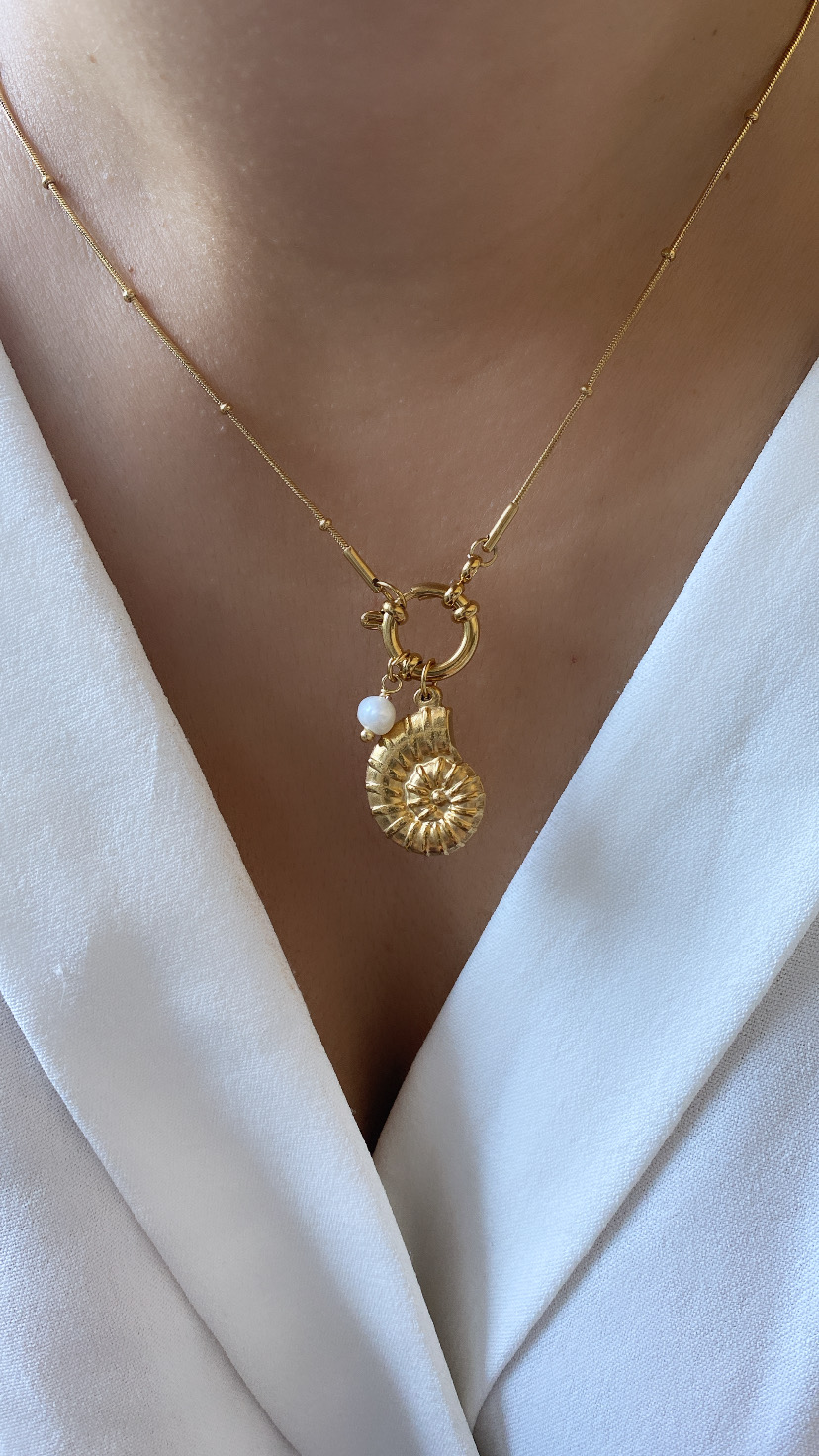 Colar dourado com pendente concha e pérola sobre blusa branca