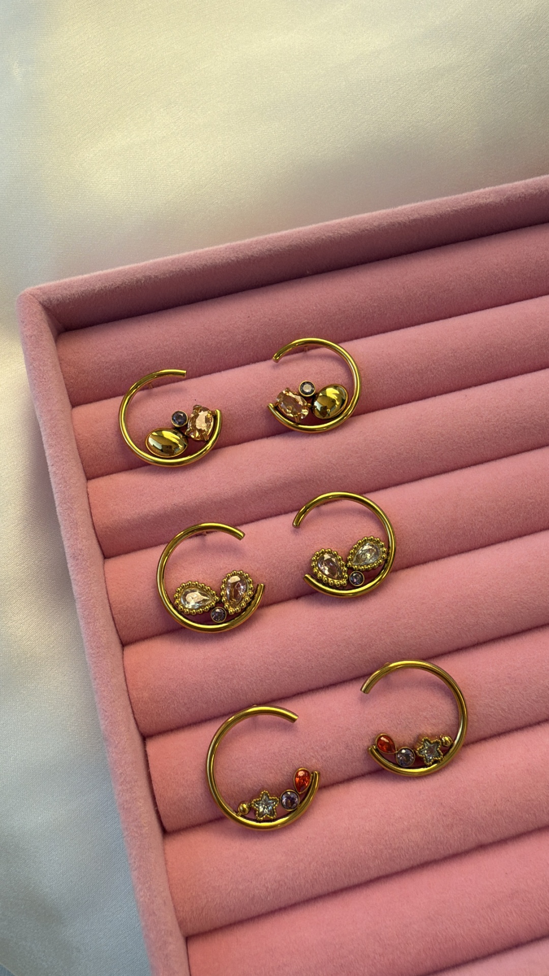 Três pares de brincos dourados com pedras numa caixa de veludo rosa