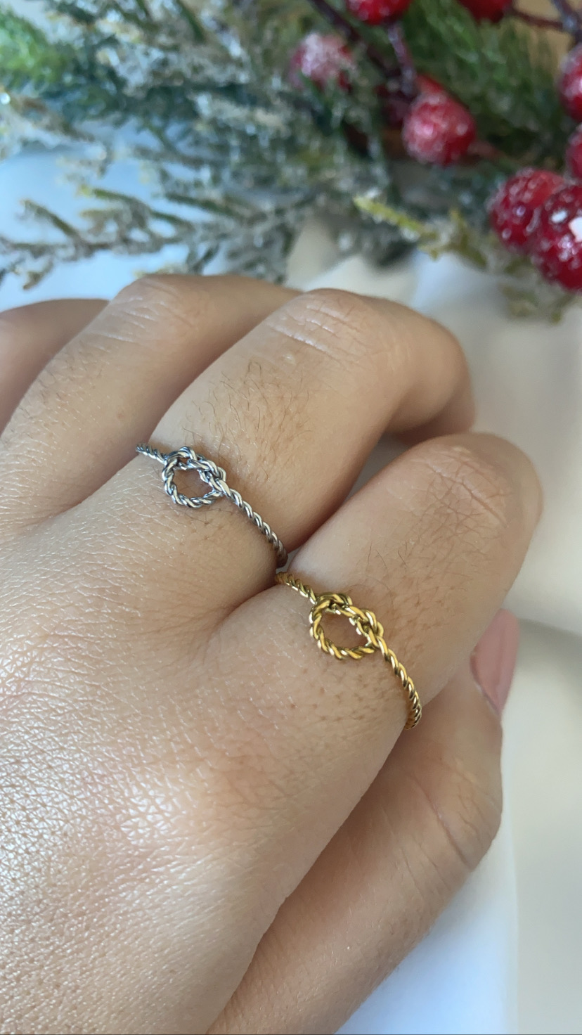 Dois anéis torcidos, um prata e outro dourado, com nó no centro em dedos da mão