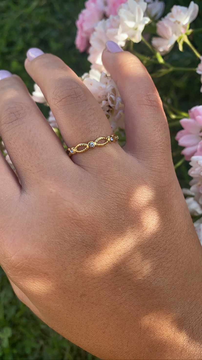 Anel dourado com pedras em mão feminina sobre flores rosas