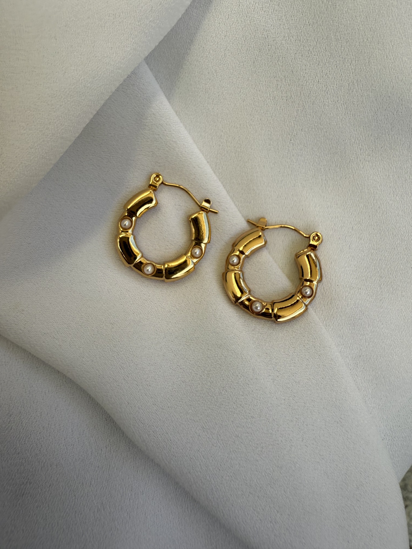 Brincos argola dourados com pérolas sobre tecido branco