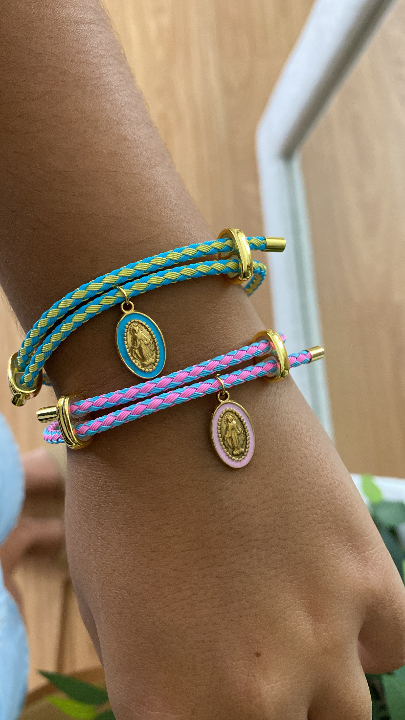 Braceletes trançados em tecido azul com amarelo e rosa com azul, com medalhas douradas penduradas no pulso