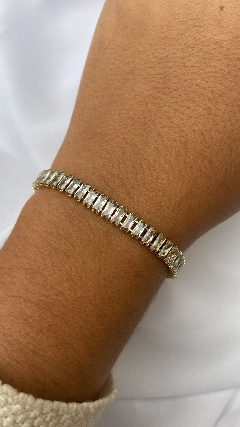 Pulseira dourada com pedras retangulares transparentes no pulso
