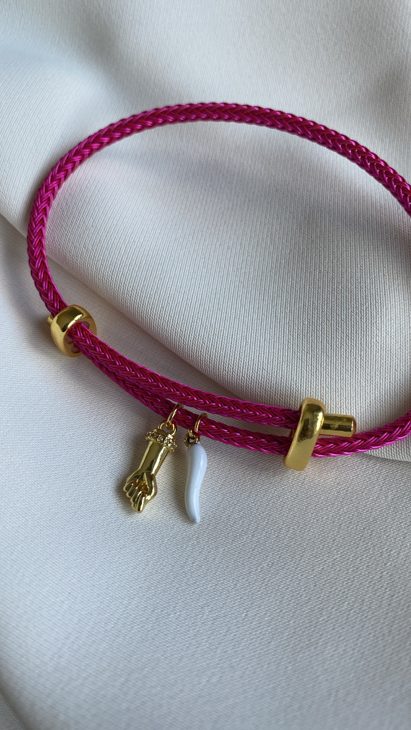 Pulseira de corda rosa com pendentes dourado e branco sobre tecido branco