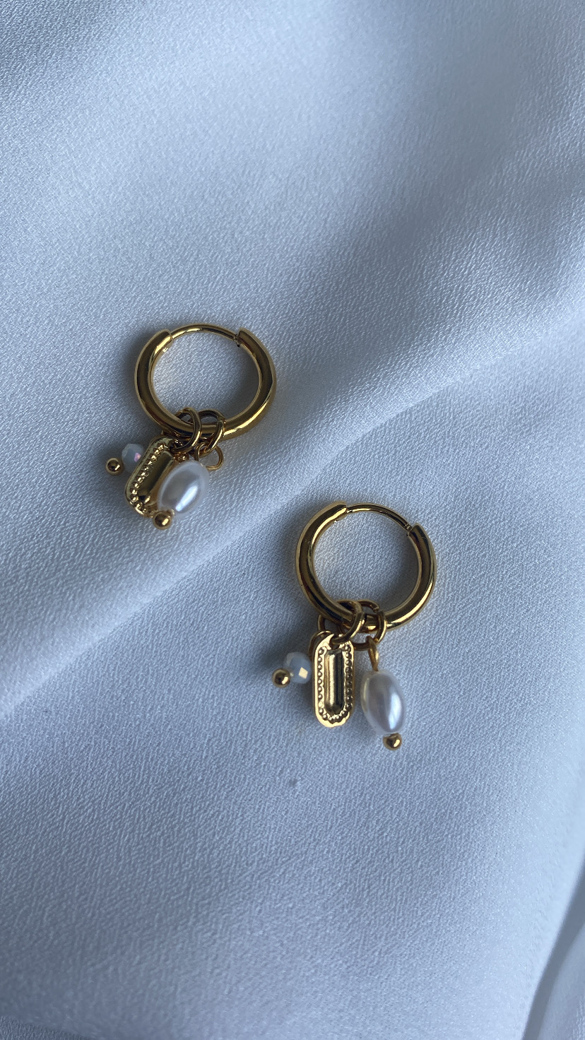 Brincos de argola dourados com pendentes de pérola e placa retangular sobre tecido branco