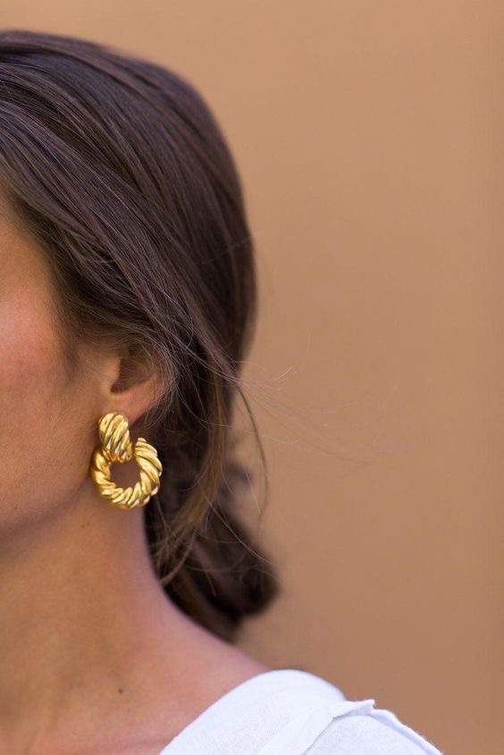 Brincos torcidos dourados em orelha de mulher com cabelo castanho