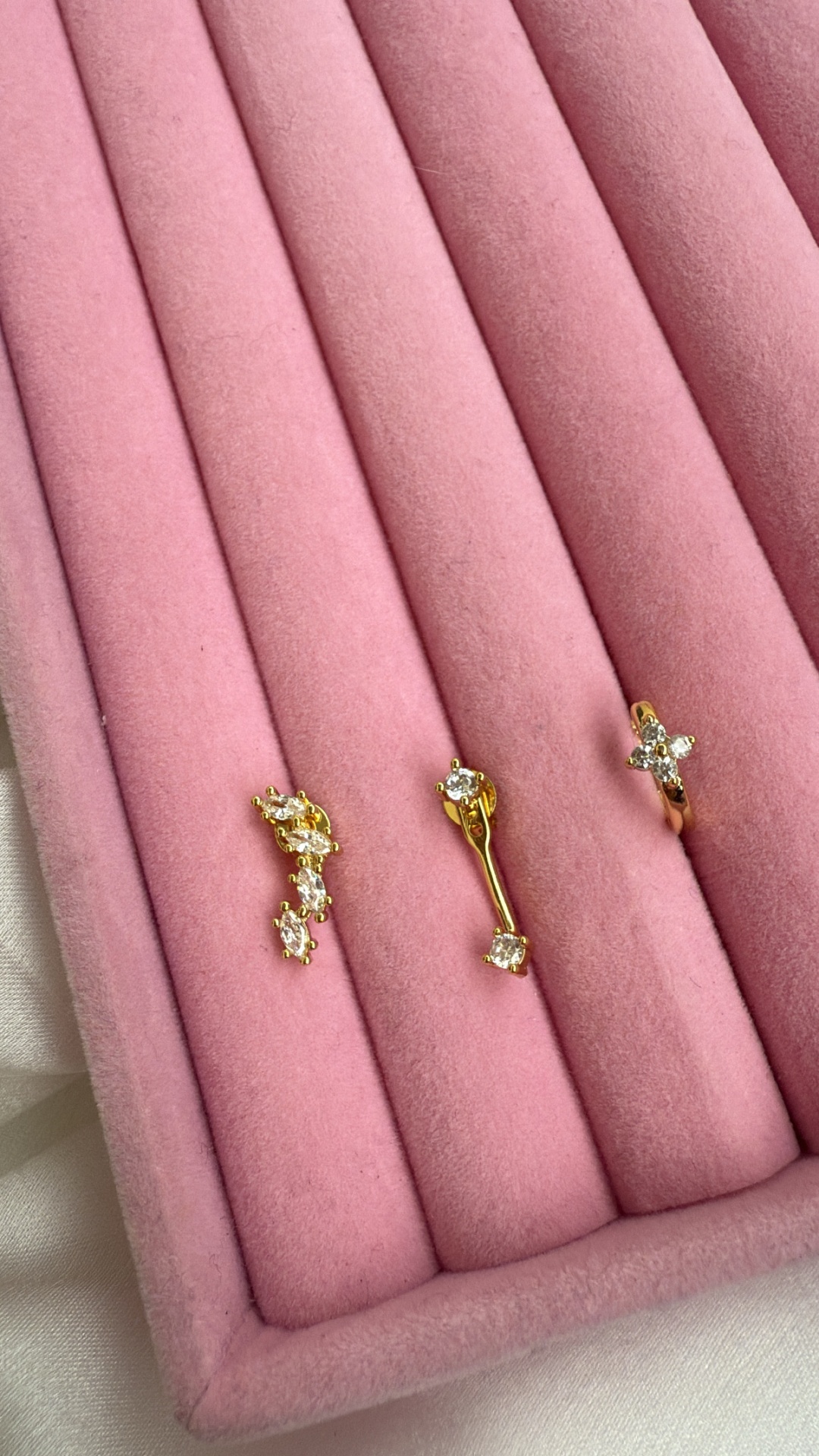 Três brincos dourados com pedras brilhantes em veludo rosa