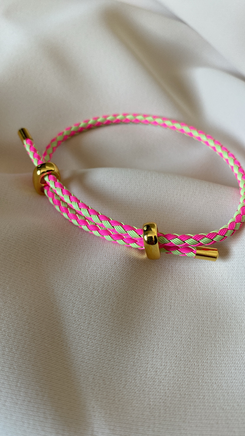 Pulseira trançada rosa, verde fluorescente e bege com detalhes dourados sobre tecido branco