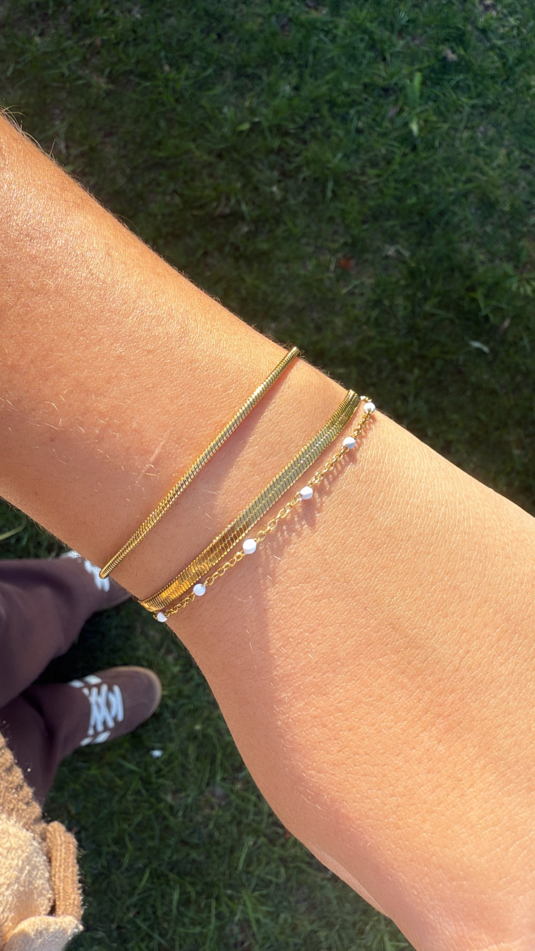 Pulseira dourada com três correntes finas e pequenas pérolas brancas ao pulso