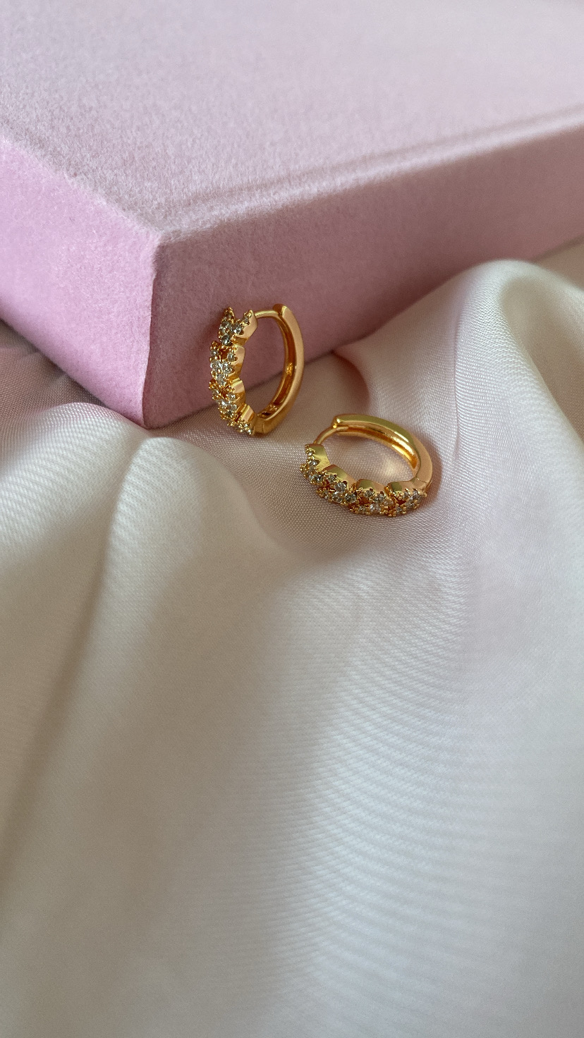 Brincos dourados com pedras em tecido branco com caixa rosa