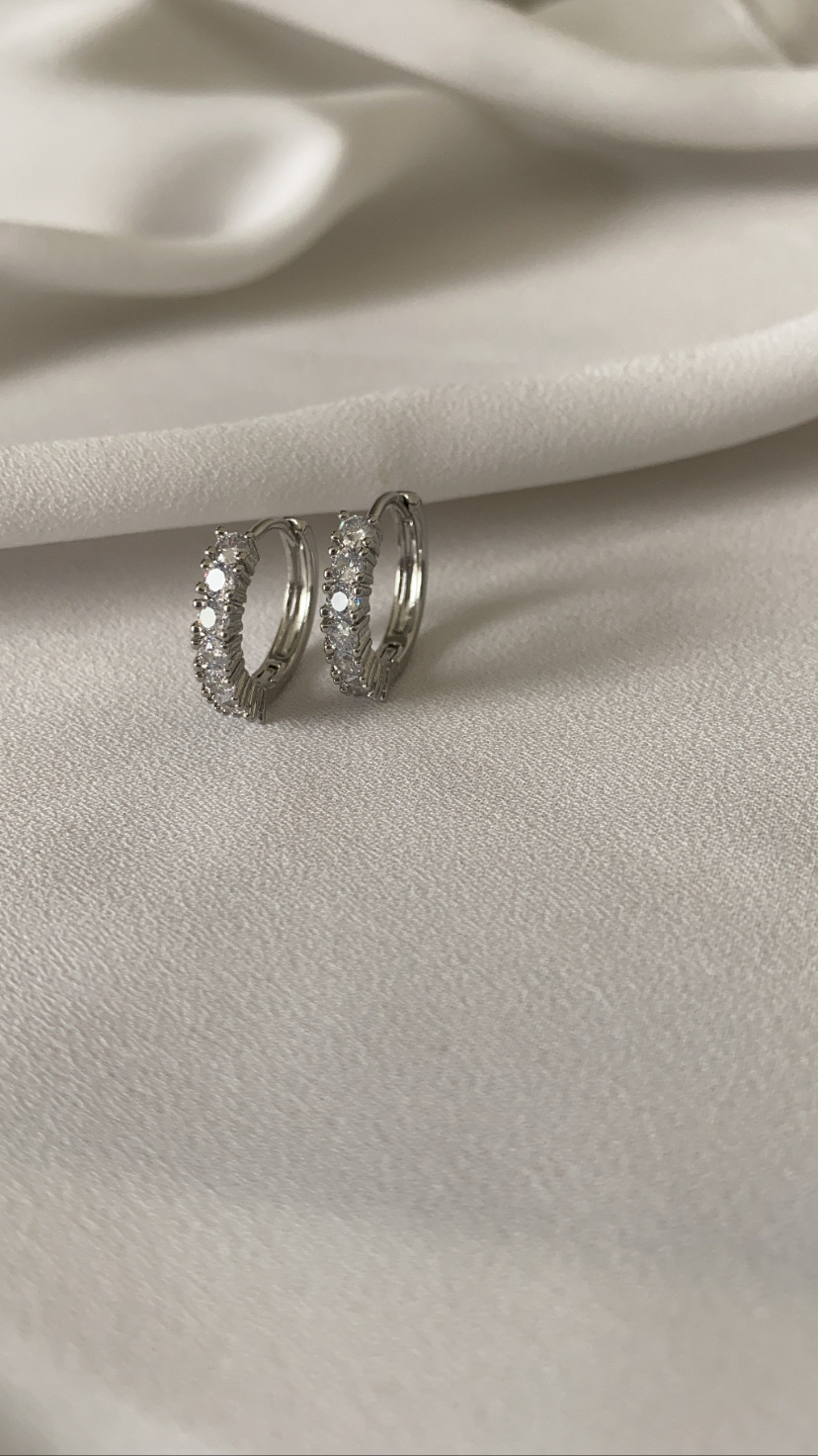 Brincos de argola pequenos em prata com pedras brilhantes sobre tecido branco