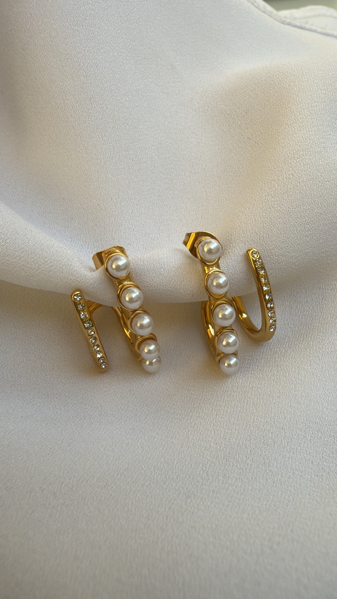 Brincos dourados com pérolas e pedras brilhantes sobre tecido branco