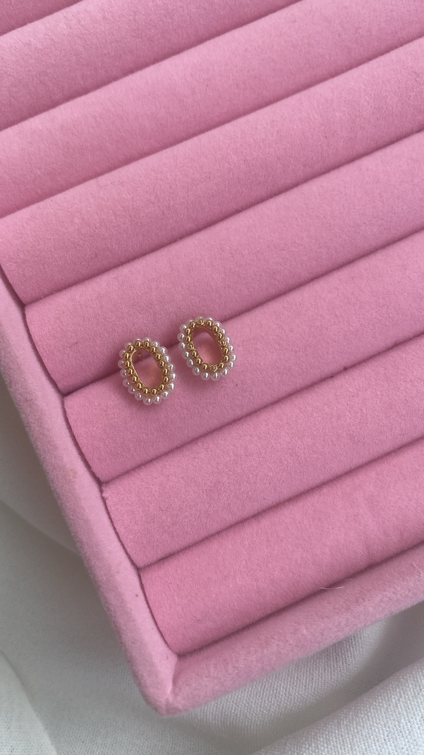 Brincos oval com pérolas e estrutura dourada numa caixa rosa de veludo.