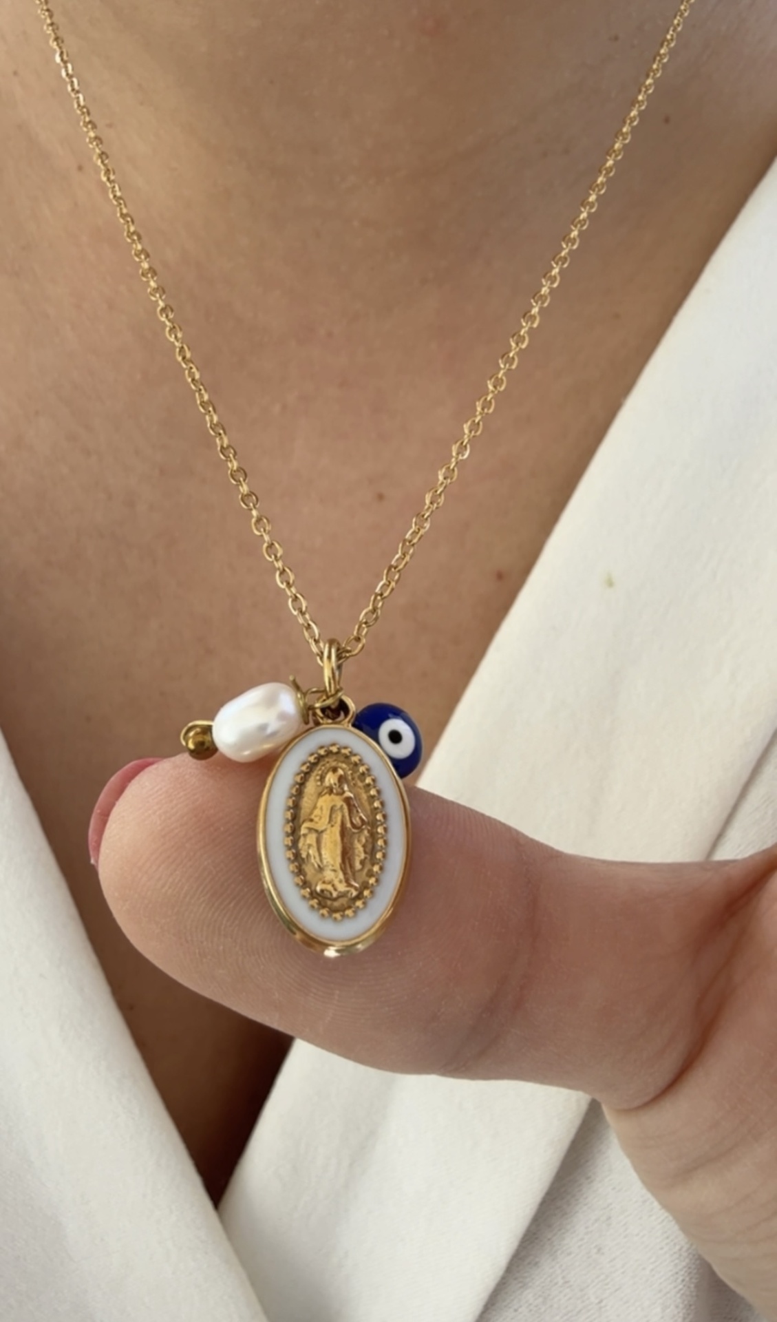 Colar dourado com pendentes de medalha religiosa, conta azul de olho e pérola