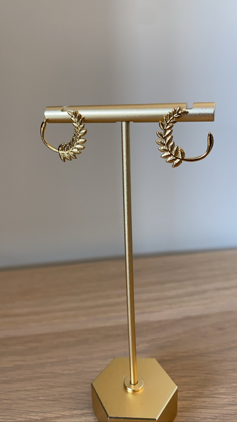 Brincos dourados com design de folhas num suporte dourado