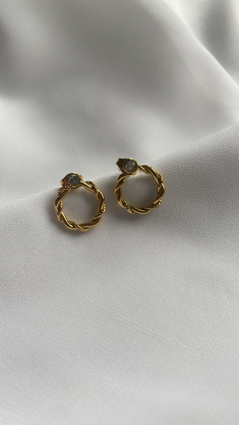 Par de brincos dourados com pedra transparente sobre tecido branco