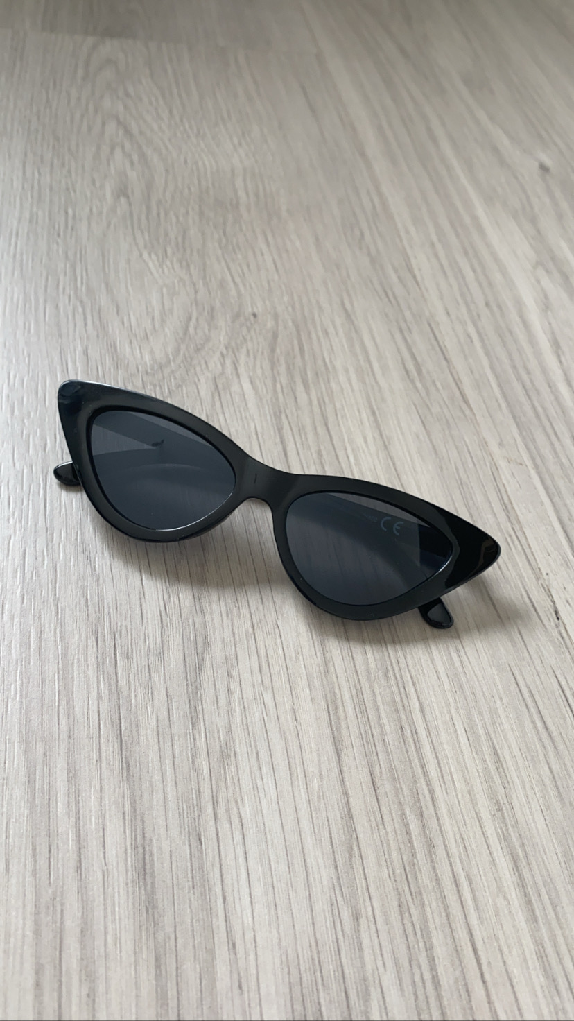 Óculos de sol pretos estilo gatinho sobre superfície de madeira clara