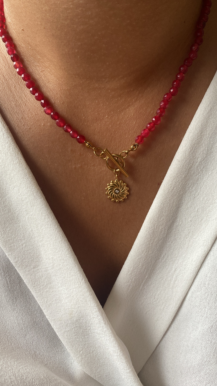 Colar com contas vermelhas e pendente dourado numa pessoa com roupa branca
