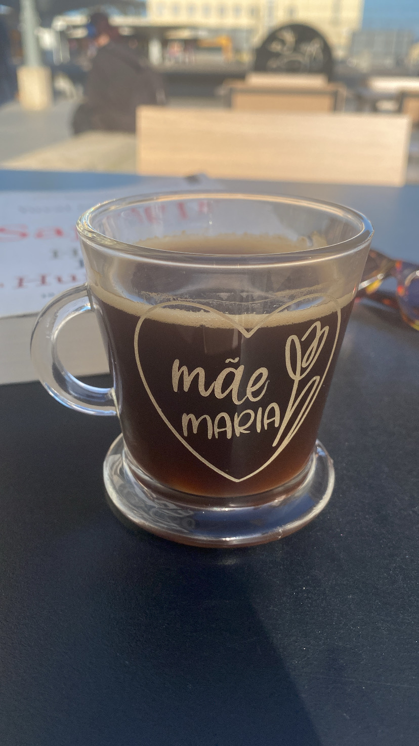 Cálice de vidro com café e texto 'mãe MARIA' impresso em branco