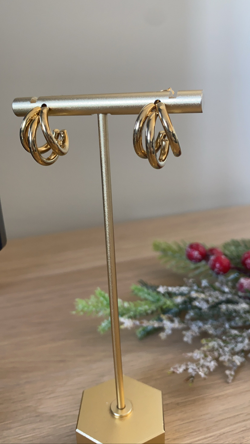 Brincos de argola dourados expostos num suporte dourado sobre mesa