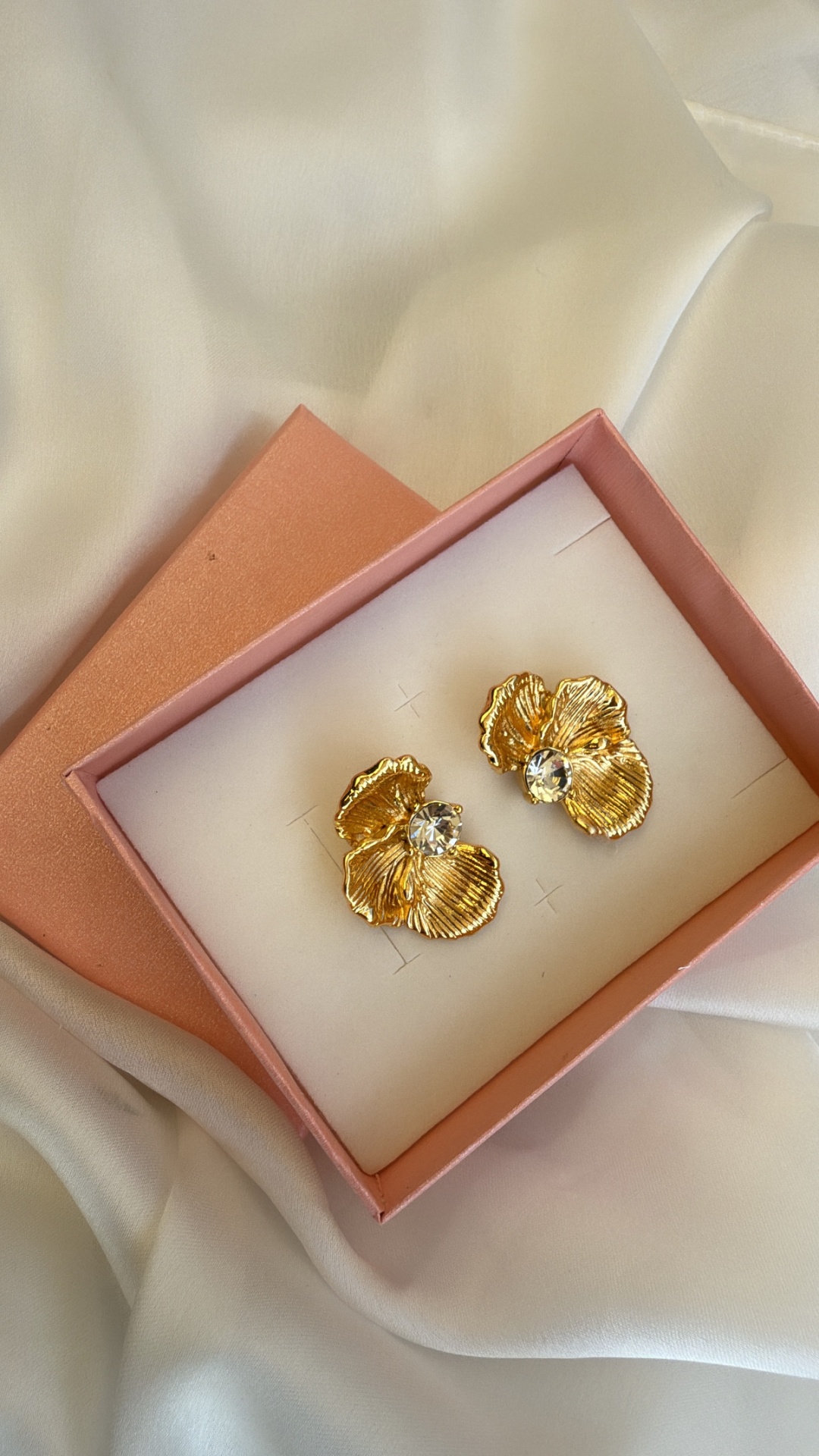 Brincos dourados com pedra brilhante em caixa cor de rosa sobre tecido branco