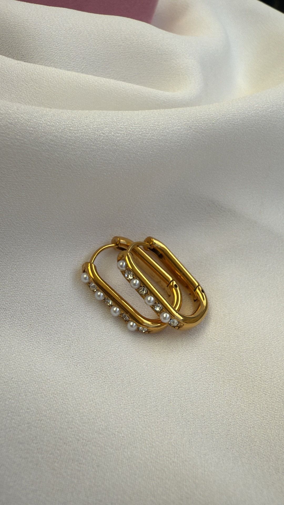 Brincos dourados retangulares com pérolas sobre tecido branco