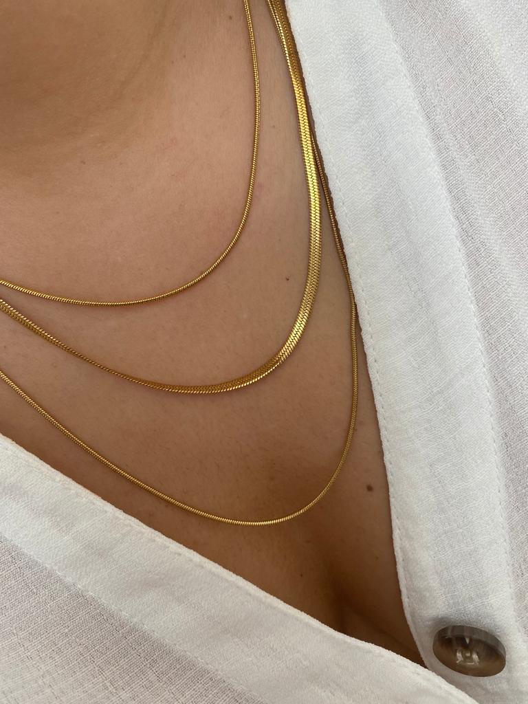 Colares dourados finos usados sobre blusa branca com botão marrom