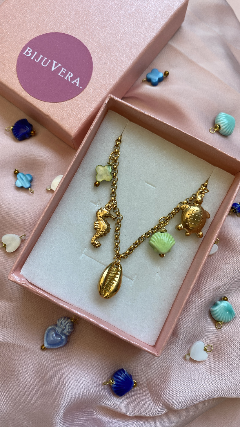 Colar dourado com pendentes marinhos em caixa rosa sobre tecido rosa