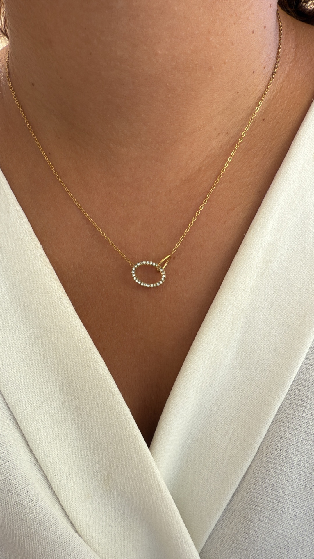 Colar dourado com pendente ovalado cravejado de pedras brancas em decote branco