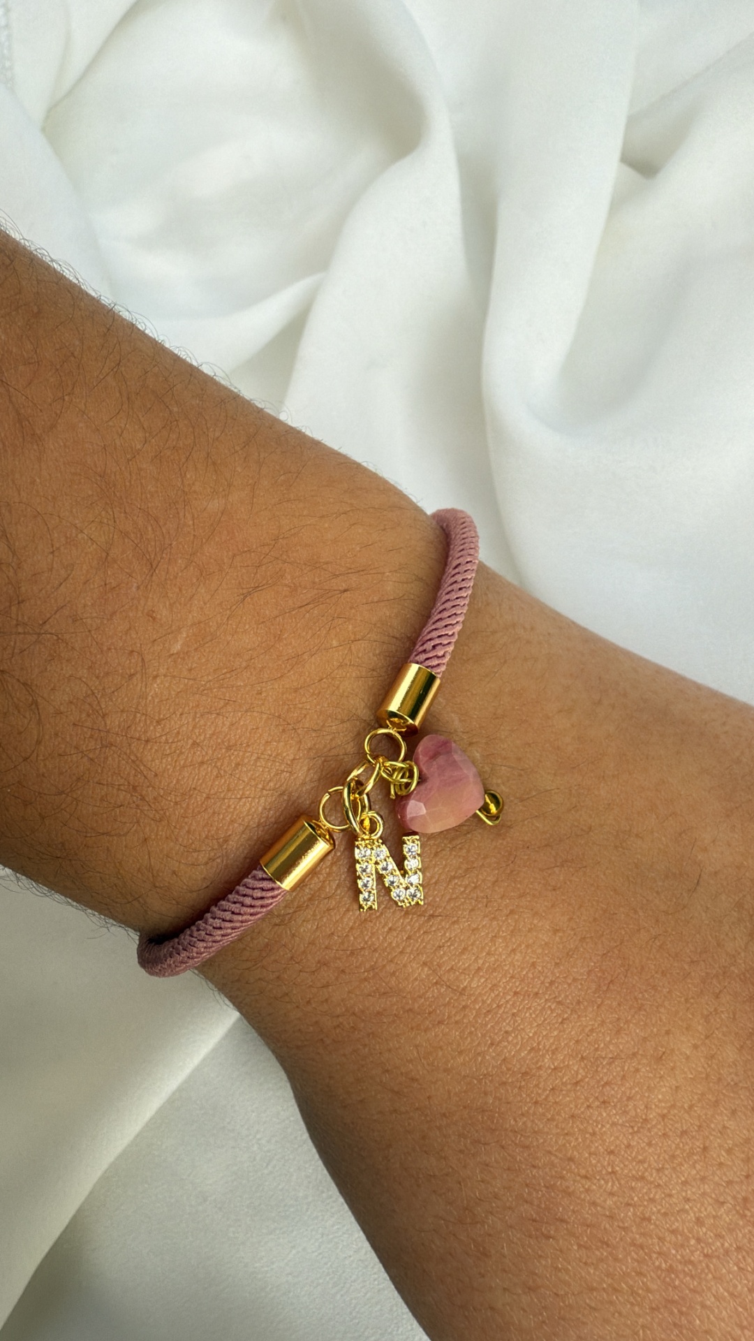 Pulseira cor-de-rosa com pendentes dourados e letra N no pulso