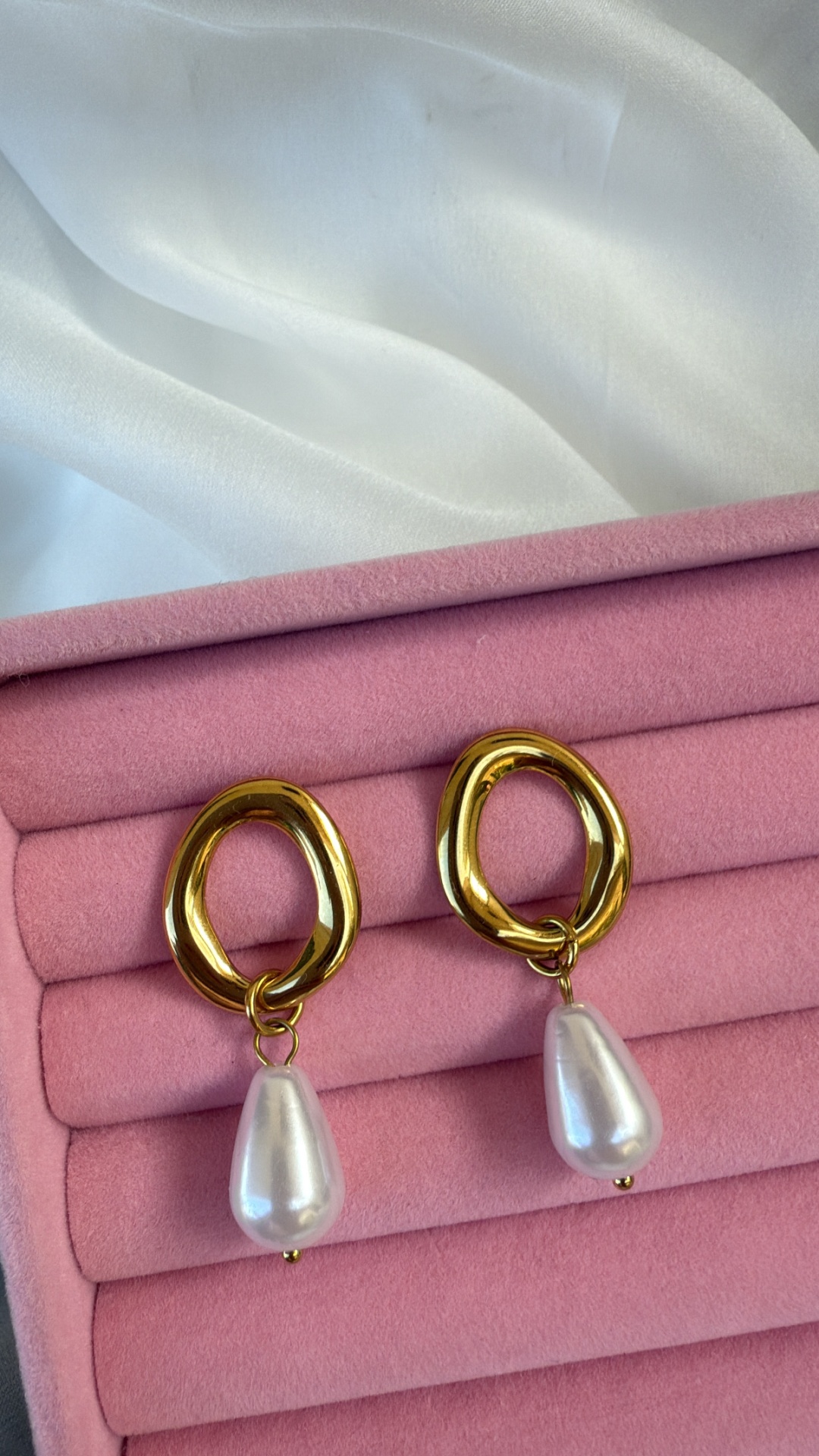 Brincos dourados com pendente de pérola numa caixa rosa